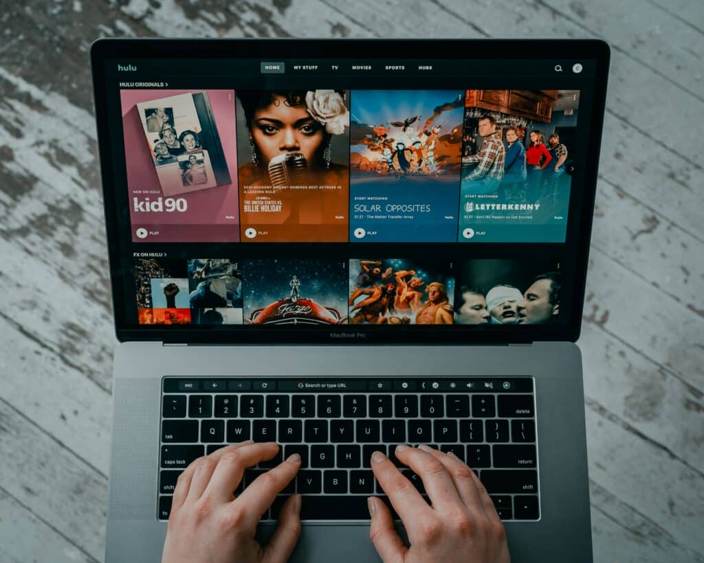 Photo of hands typing on a Macbook pro keyboard, with the screen displaying Hulu