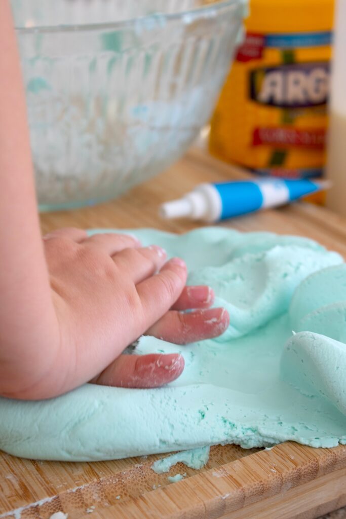 toddler hands smushing cloud dough on a cutting board