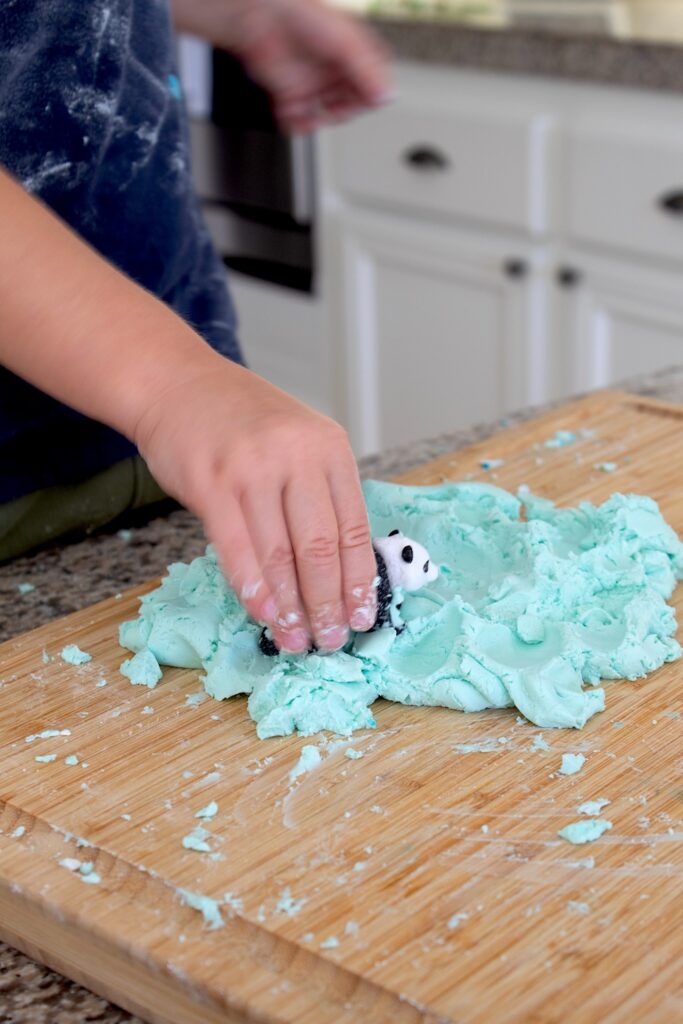 toddler hands playing with a toy panda in cloud dough