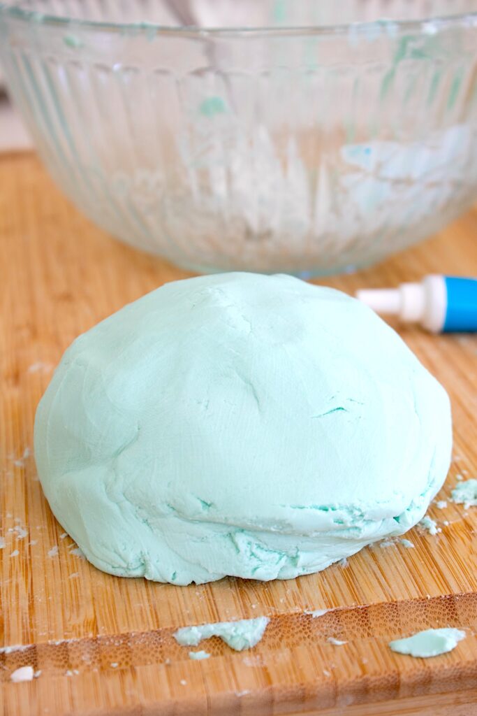 ball of cloud play dough on a cutting board with food coloring in background