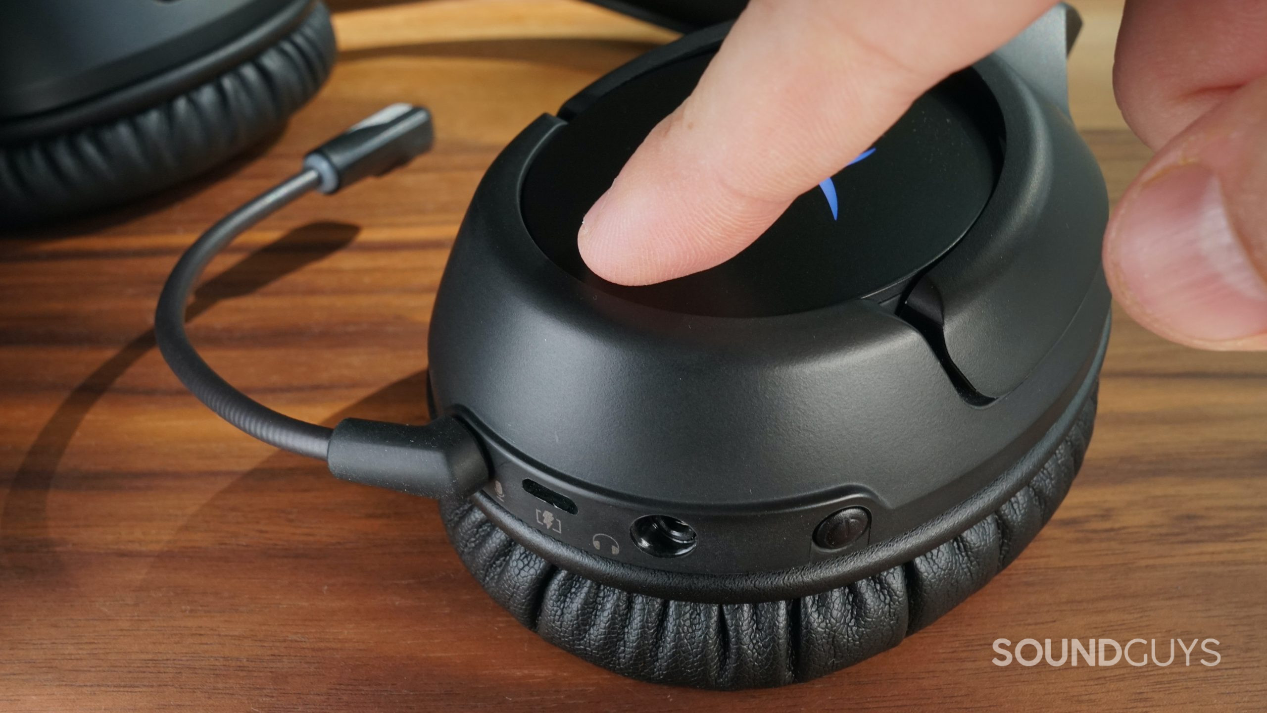 A hand presses the mic mute button on the side of the HyperX Cloud Flight Wireless